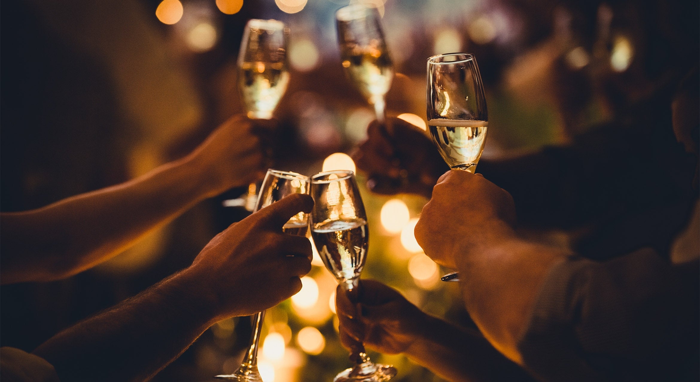 A set of hands holding up champagne flutes in a cheers at night