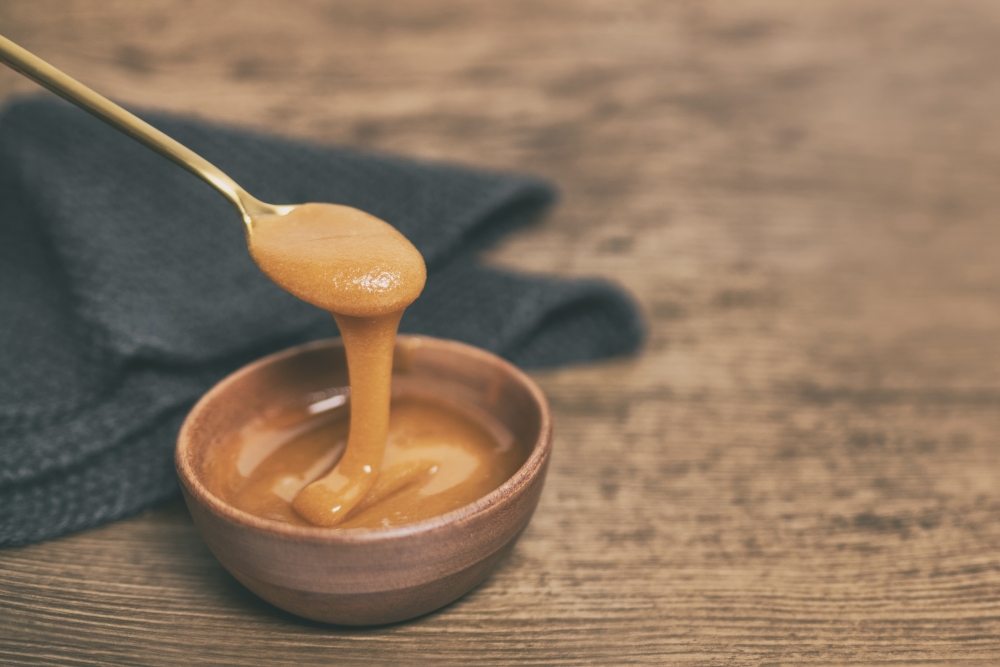 A spoon drizzling manuka honey into a wooden bowl
