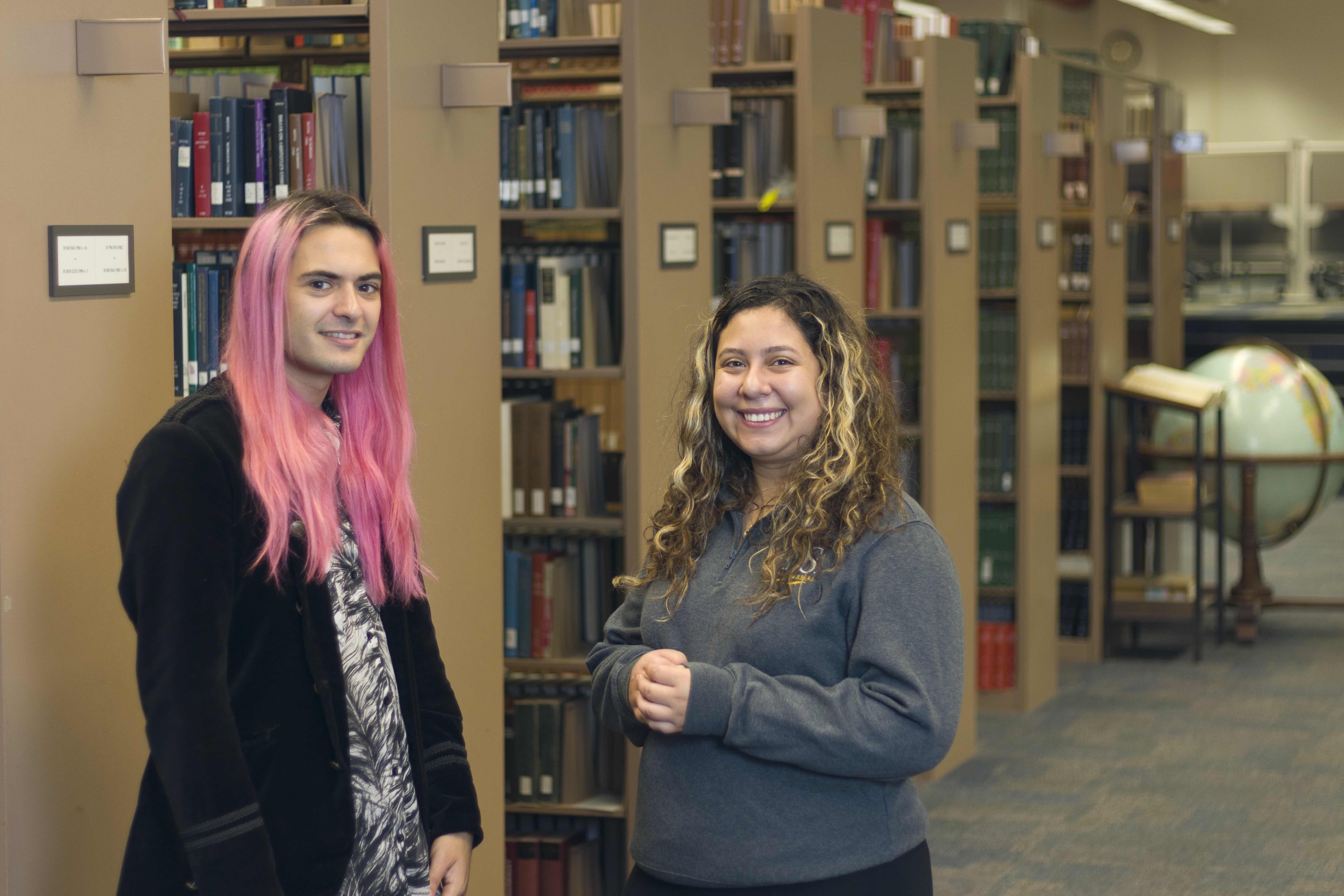 two students stand near library stacks