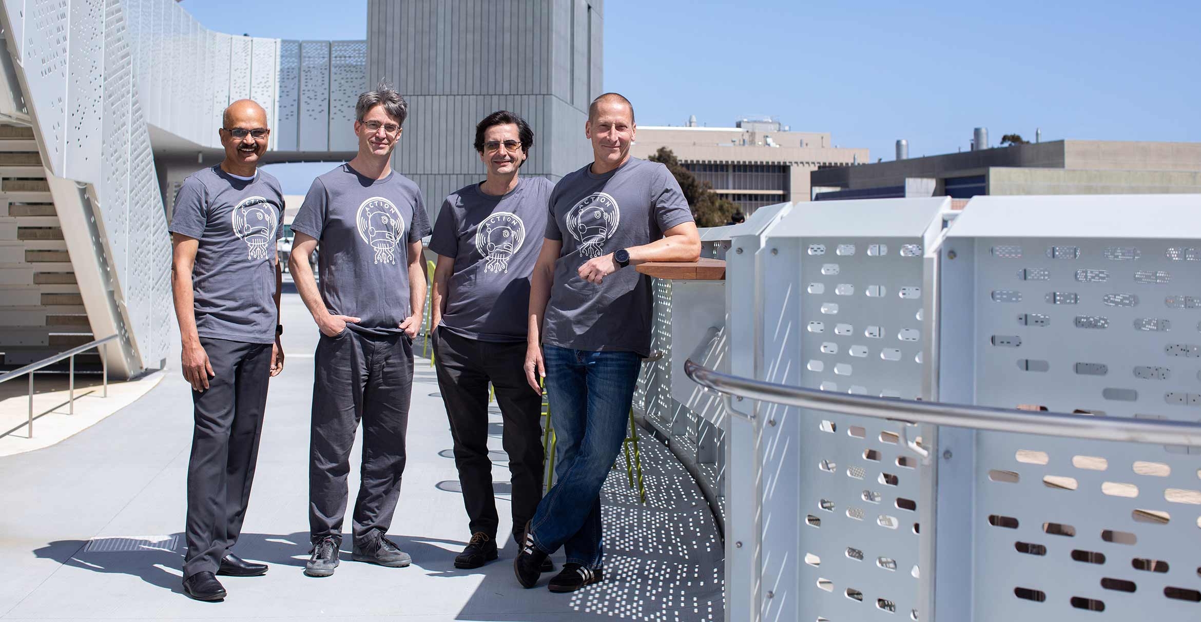 group of researchers in gray t-shirts standing outside a modern building