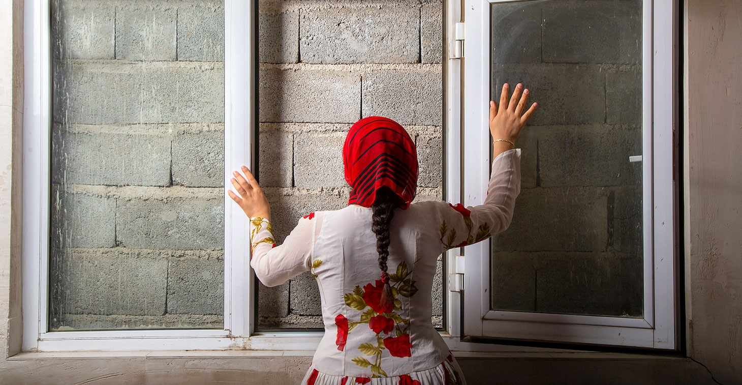 A woman seen from behind standing a window that opens to a brick wall