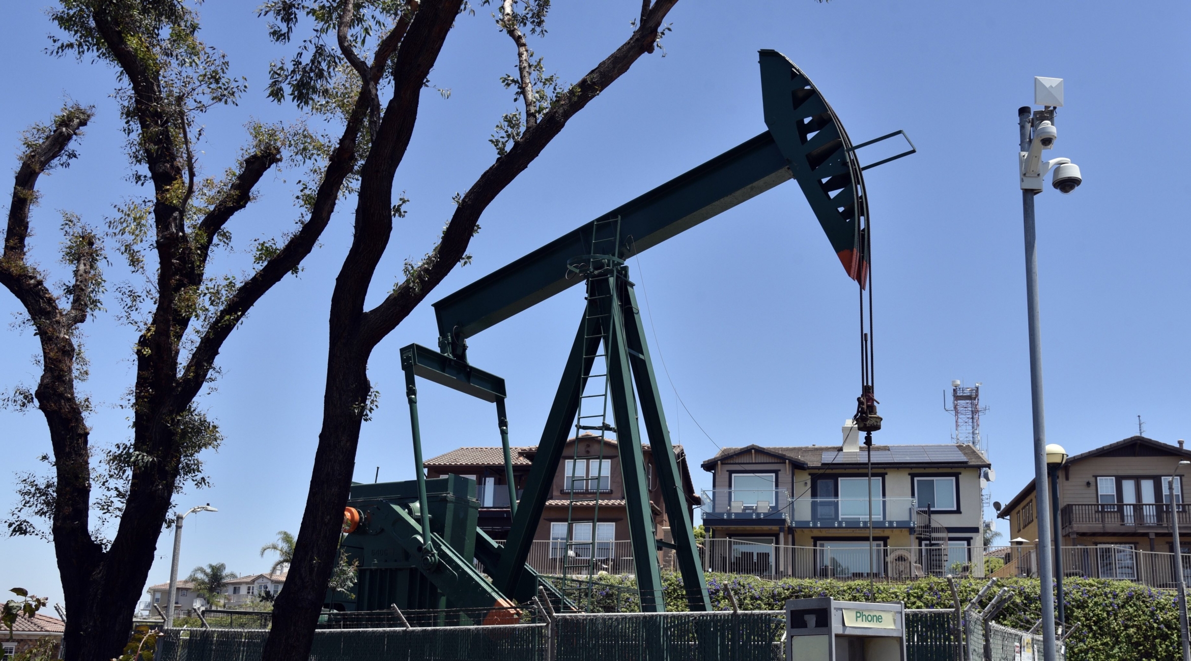 A pumpjack nestled between trees and luxury homes.
