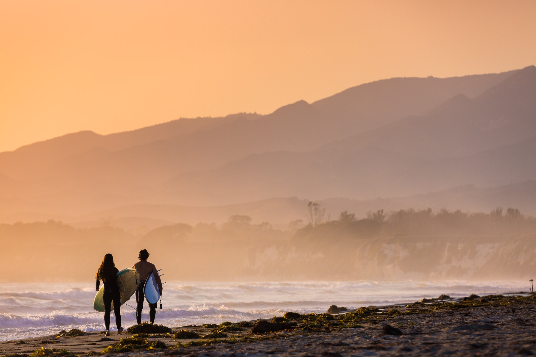 two surfers walking the beach at sunset