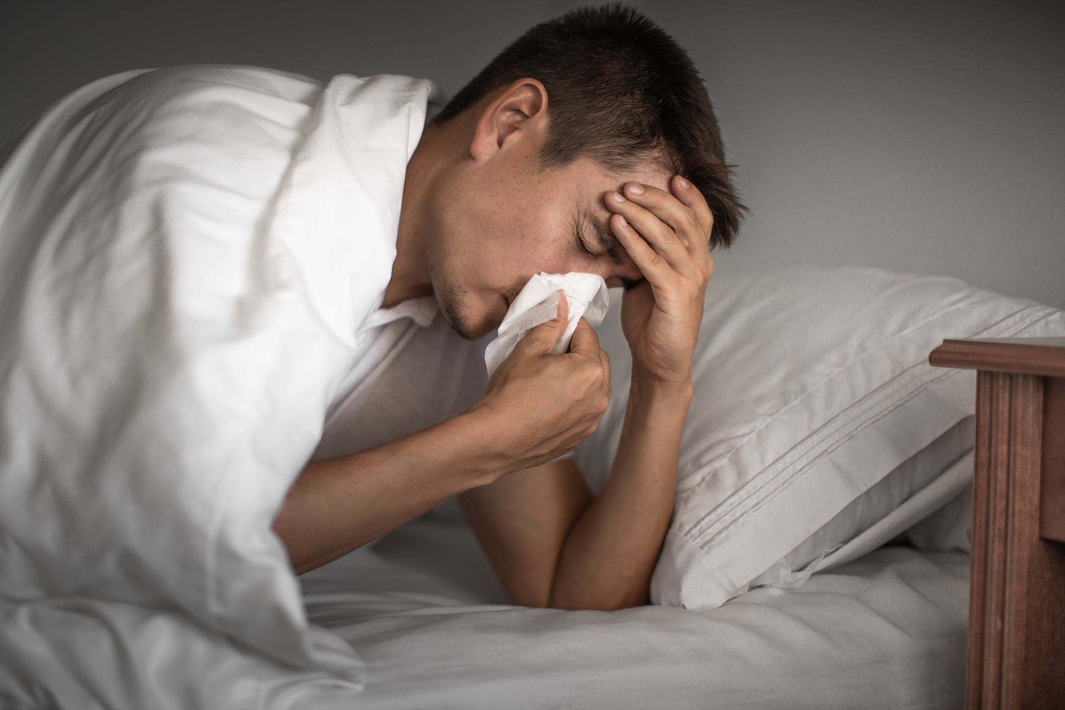 man sneezing in bed