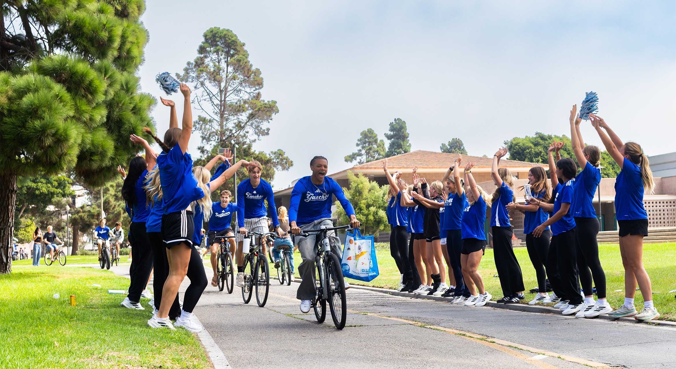 Adults in blue t-shirts ride bikes through cooridor of adults in blue t-shirt with arms upraised