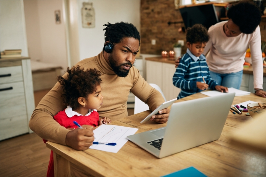 Young father trying to work on laptop as his children stand around him